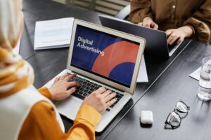 Two professionals work on laptops focusing on digital advertising in an office setting.